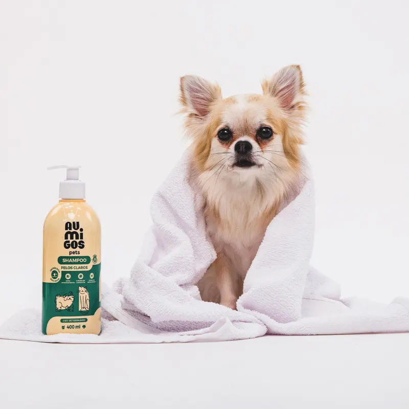 Shampoo Pelos Claros Au.Migos Pets no canto; ao lado, um cachorro de pelagem clara enrolado em uma toalha